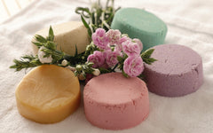 Colorful all-natural plastic-free shampoo bars arranged with fresh flowers on a white towel.