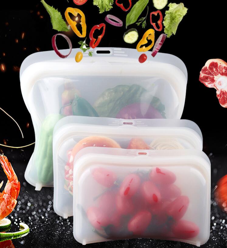 Three clear reusable silicone food bags in different sizes filled with fresh vegetables and cherry tomatoes.