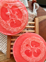 natural loofah soap bar displayed on a wooden rack showcasing its peach color and loofah texture.