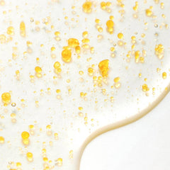 Brightening body serum mist with yellow serum droplets on a smooth surface for skincare hydration.
