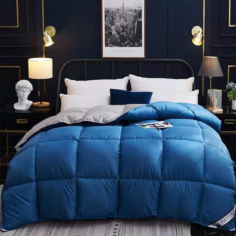 Cozy blue winter goose down duvet neatly spread on a bed with white and blue pillows in a stylish bedroom.