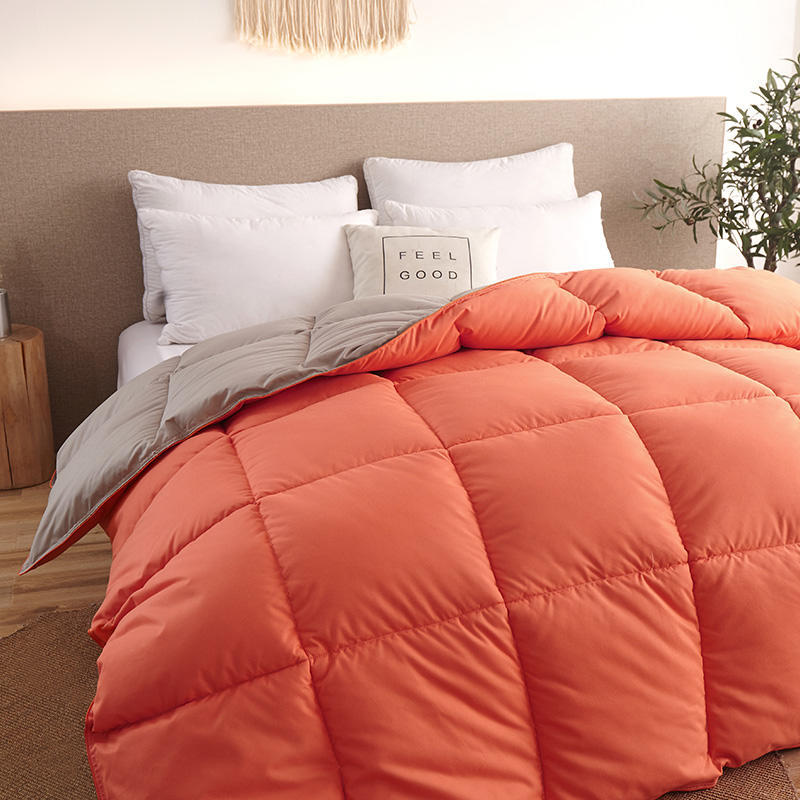 An orange winter goose down duvet neatly spread on a bed with white pillows.