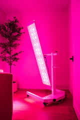 Versatile light therapy panel in a modern room, featuring adjustable stand and vibrant pink light.