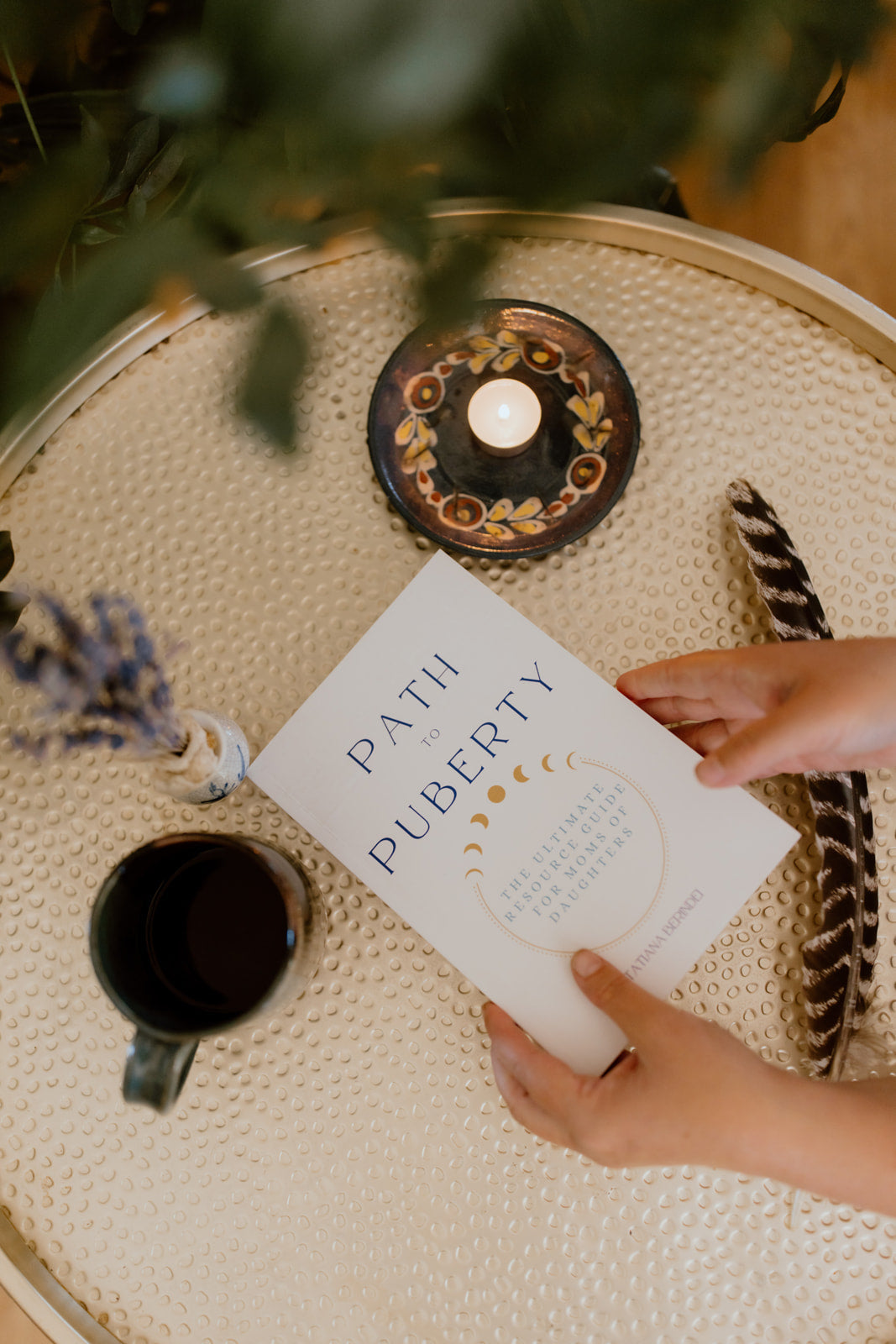 Hands holding the Path to Puberty book on a table with a candle, showcasing a puberty guide for girls.