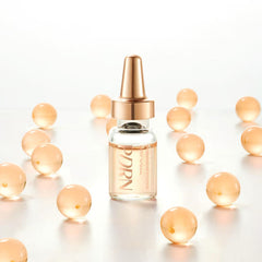 salmon PDRN ampoule for hydration in a clear glass bottle surrounded by peach-colored spherical capsules.